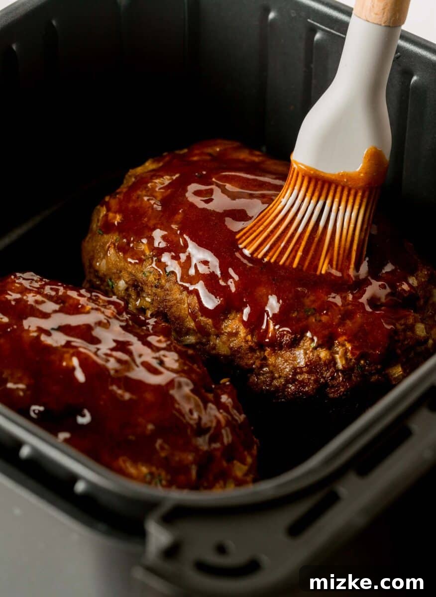 A silicone pastry brush evenly applying a thick, glossy layer of meatloaf glaze over the cooking meatloaf.