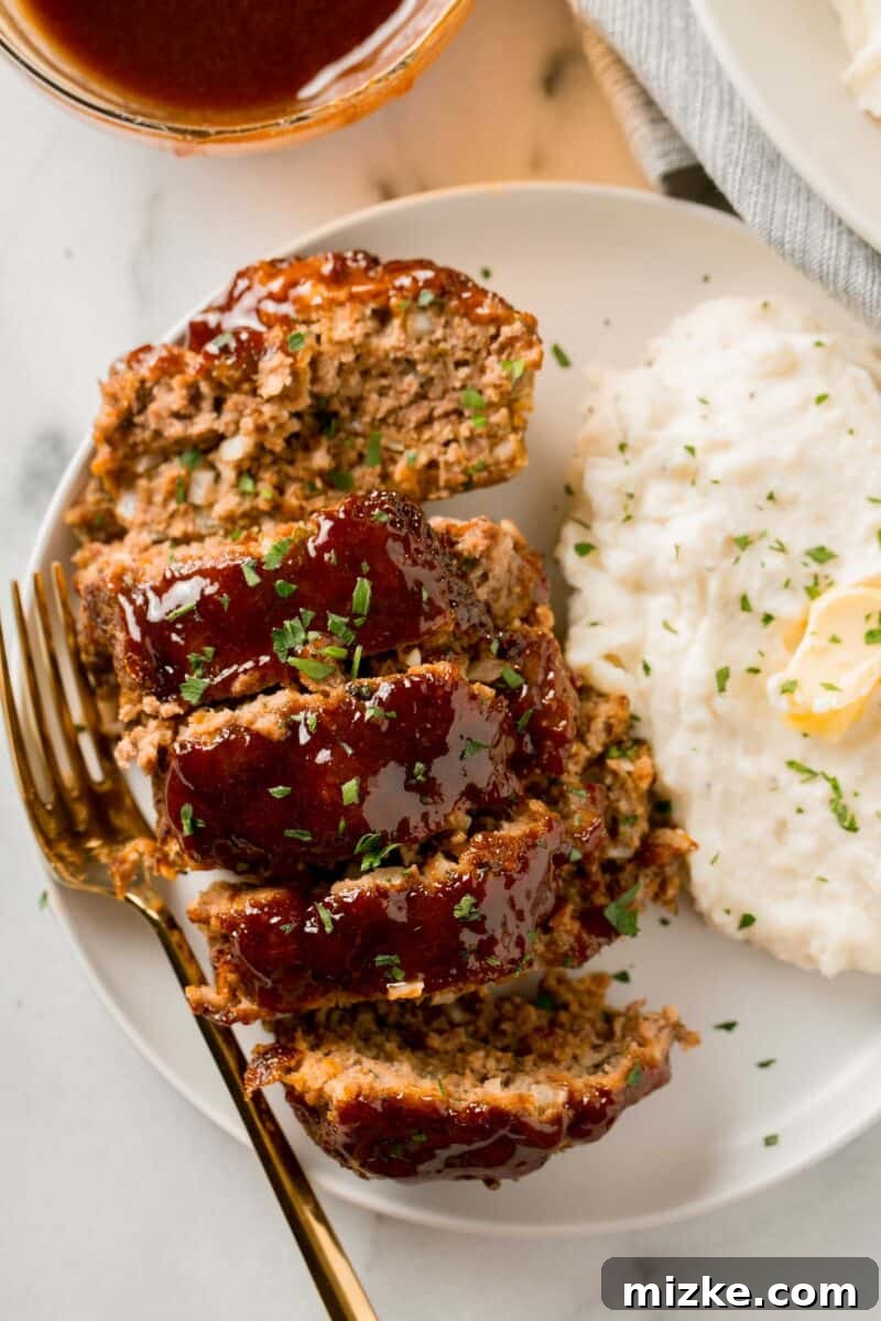 An overhead view of perfectly sliced meatloaf, garnished with fresh parsley, served alongside a fluffy mound of mashed potatoes.