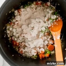 Hearty Stovetop Chicken and Dumplings with Biscuits 10 Flour sprinkled on top of the vegetable mixture in the Dutch oven, being stirred with a wooden spoon.