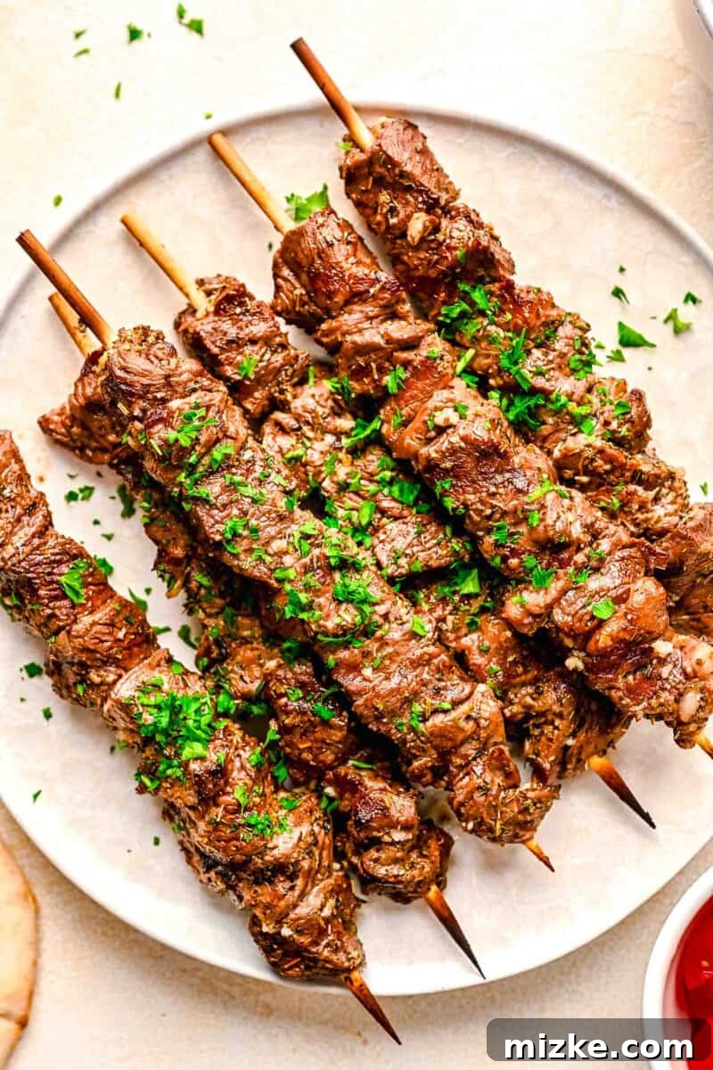 Skewered beef souvlaki on a white plate with fresh parsley sprinkled on top as garnish