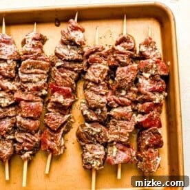 Beef pieces skewered on wooden skewers and placed on a metal baking sheet, ready for the grill.