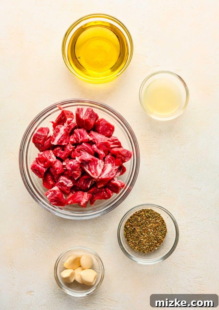 Ingredients for beef souvlaki laid out on a table, including olive oil, lemon, garlic, Greek seasoning, and cubed chuck roast.