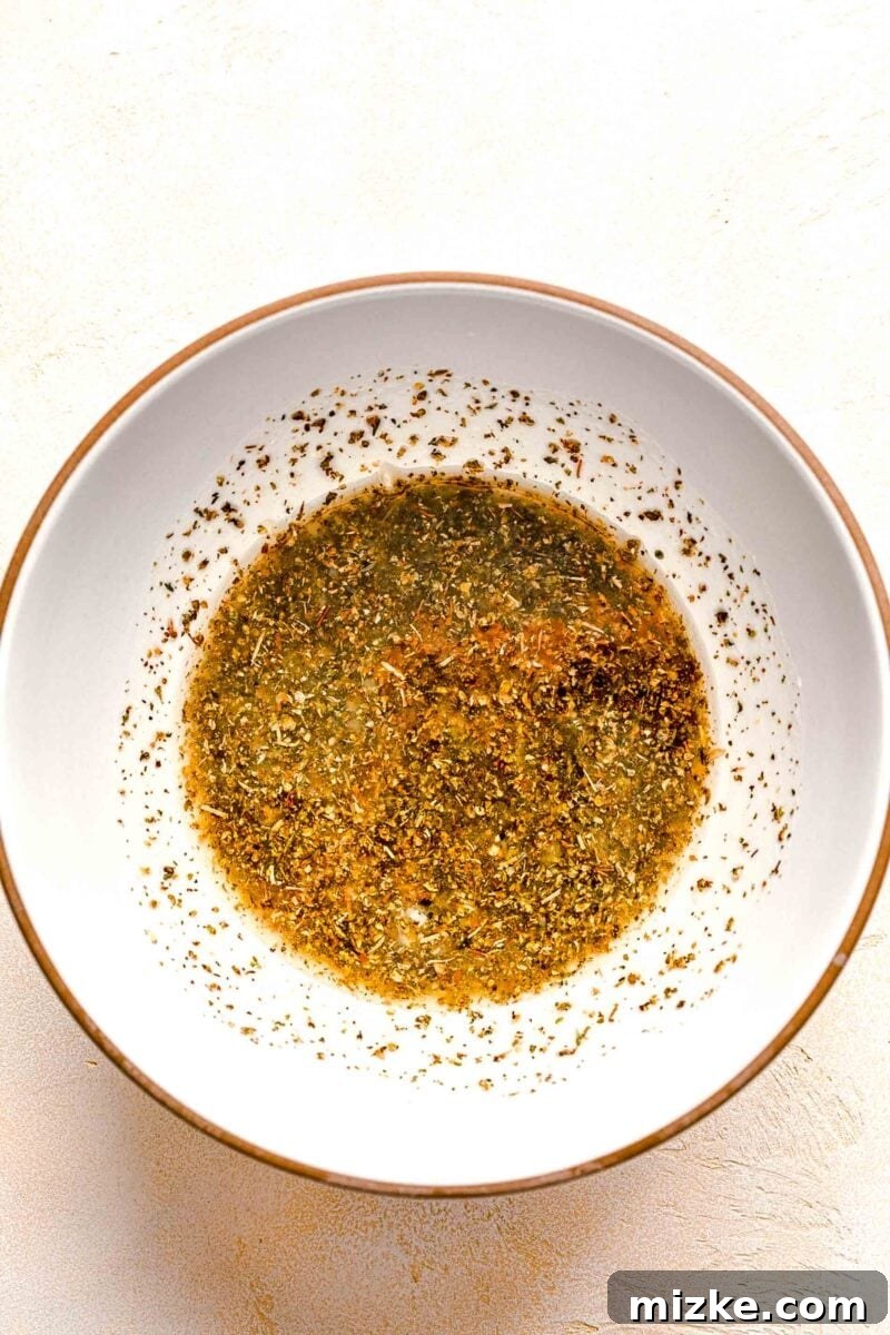 Marinade for beef souvlaki mixed together in a white ceramic bowl, showcasing the olive oil, lemon juice, garlic, and Greek seasoning.