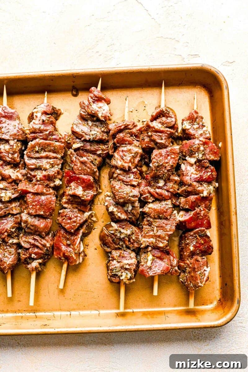 Beef pieces skewered on wooden skewers and placed on a metal baking sheet, ready for grilling.