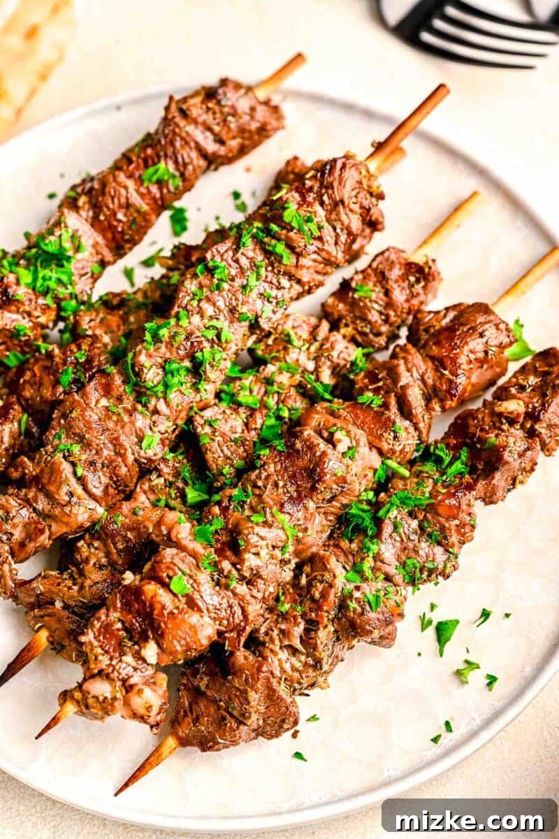 Grilled beef souvlaki on wooden skewers on a white plate with fresh parsley sprinkled on top, ready to serve.