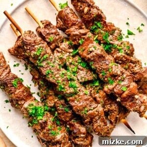 Skewered beef souvlaki on a white plate with fresh parsley sprinkled on top as garnish