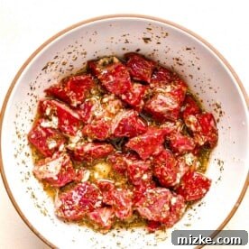Beef cubes tossed in the Greek marinade, showing the marinating process.
