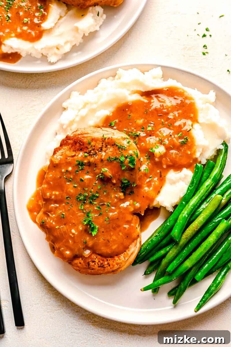 Perfectly Tender Instant Pot Pork Chops 2 Pork chop loin on a bed of mashed potatoes with savory gravy on top, next to freshly cooked green beans