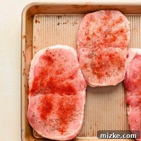 Perfectly Tender Instant Pot Pork Chops 12 Raw pork chops on a metal sheet pan with seasonings sprinkled on top