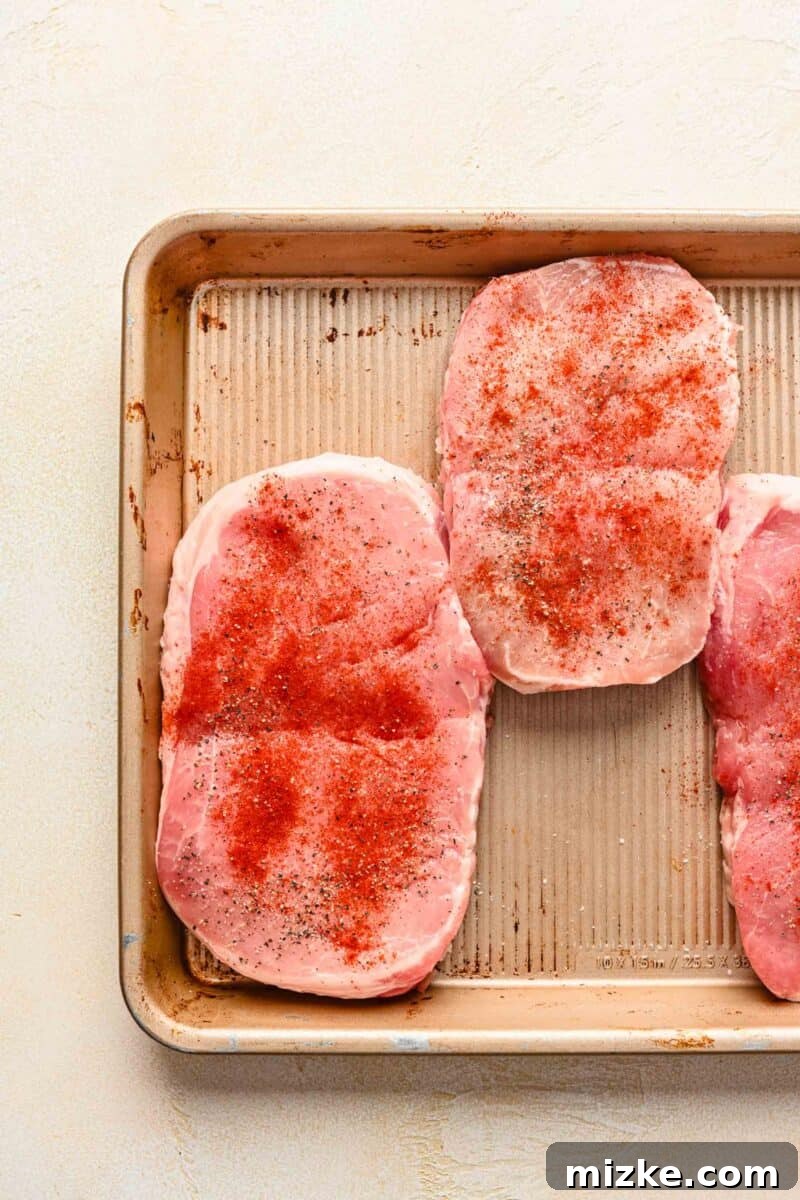 Perfectly Tender Instant Pot Pork Chops 4 Raw boneless pork chops seasoned with salt, pepper, and smoked paprika on a metal sheet pan