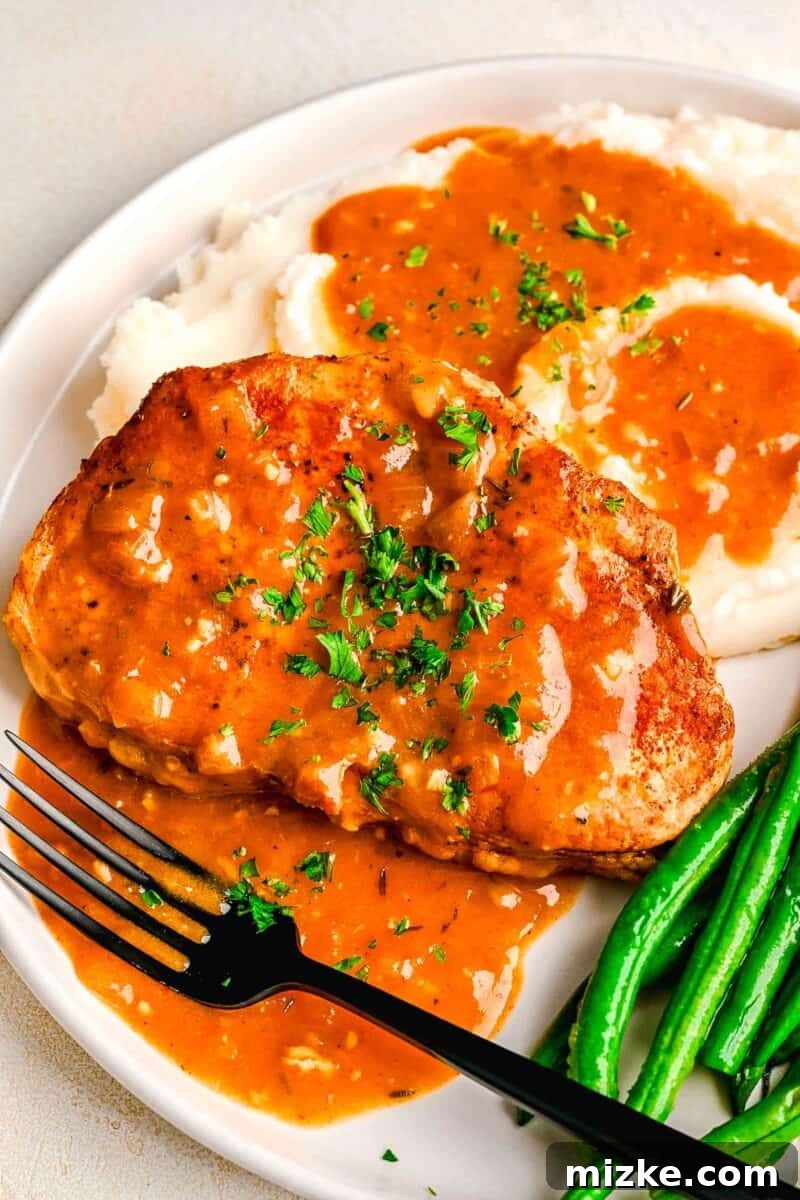 Perfectly Tender Instant Pot Pork Chops 9 Perfectly cooked pork chops served alongside creamy mashed potatoes and vibrant green beans, all generously topped with homemade pan gravy