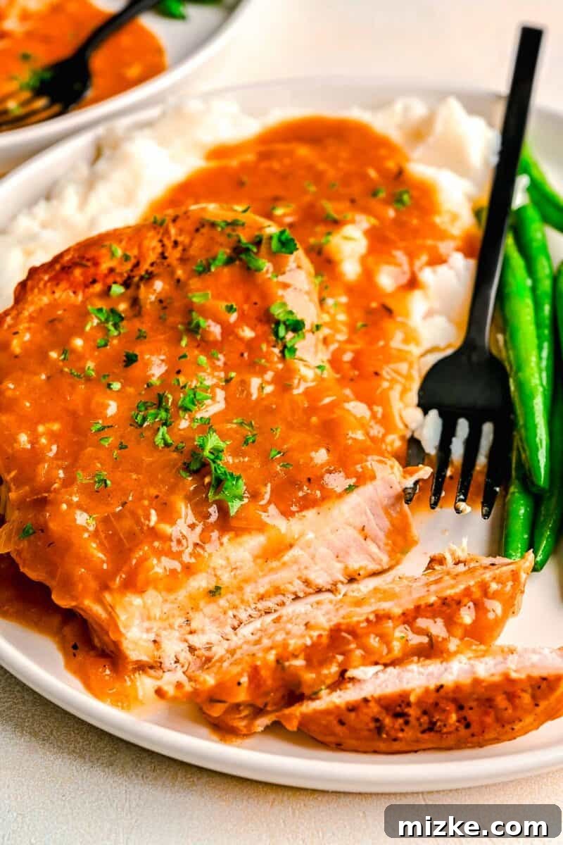 Perfectly Tender Instant Pot Pork Chops 10 Sliced pieces of tender pork chop with rich gravy on a white plate, accompanied by a black fork