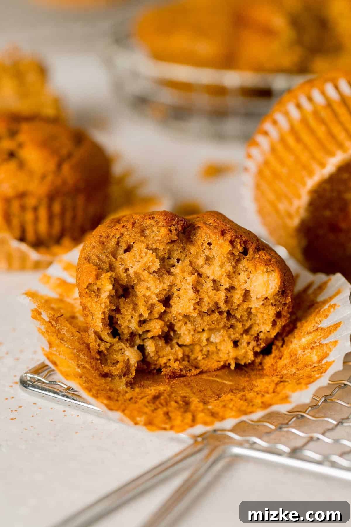 The perfect Fall baking treat, these pumpkin banana muffins are bouncy, tender, and oh-so-moist. You will absolutely fall in love with these! A perfectly baked pumpkin banana muffin, partially unwrapped from its paper liner, reveals a fluffy, moist, and tender interior, with a bite playfully missing.