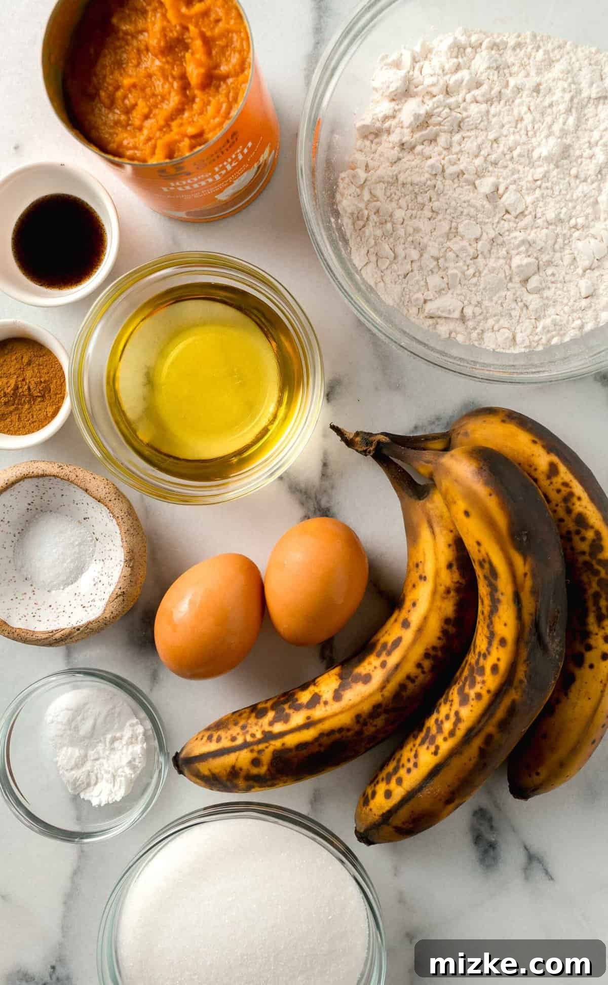 The perfect Fall baking treat, these pumpkin banana muffins are bouncy, tender, and oh-so-moist. You will absolutely fall in love with these! A vibrant display of fresh ingredients laid out, ready for making pumpkin banana muffins, including ripe bananas, a can of pumpkin puree, flour, sugar, and various spices.