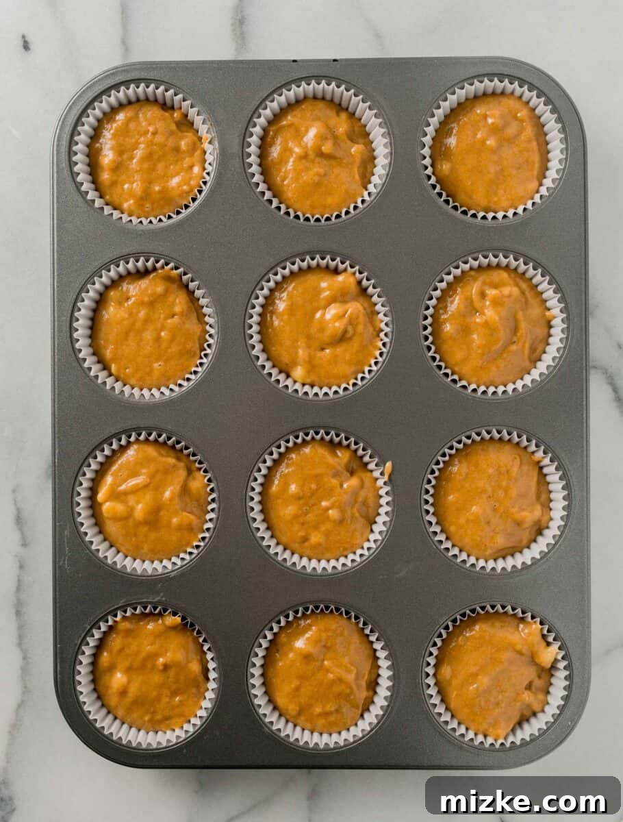 The perfect Fall baking treat, these pumpkin banana muffins are bouncy, tender, and oh-so-moist. You will absolutely fall in love with these! A lined 12-well metal muffin tin is uniformly filled with pumpkin banana muffin batter, ready for baking.