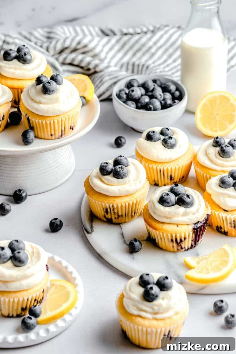 lemon blueberry cupcakes on marble plates and cake platters with fresh blueberries in a bowl and a milk jug