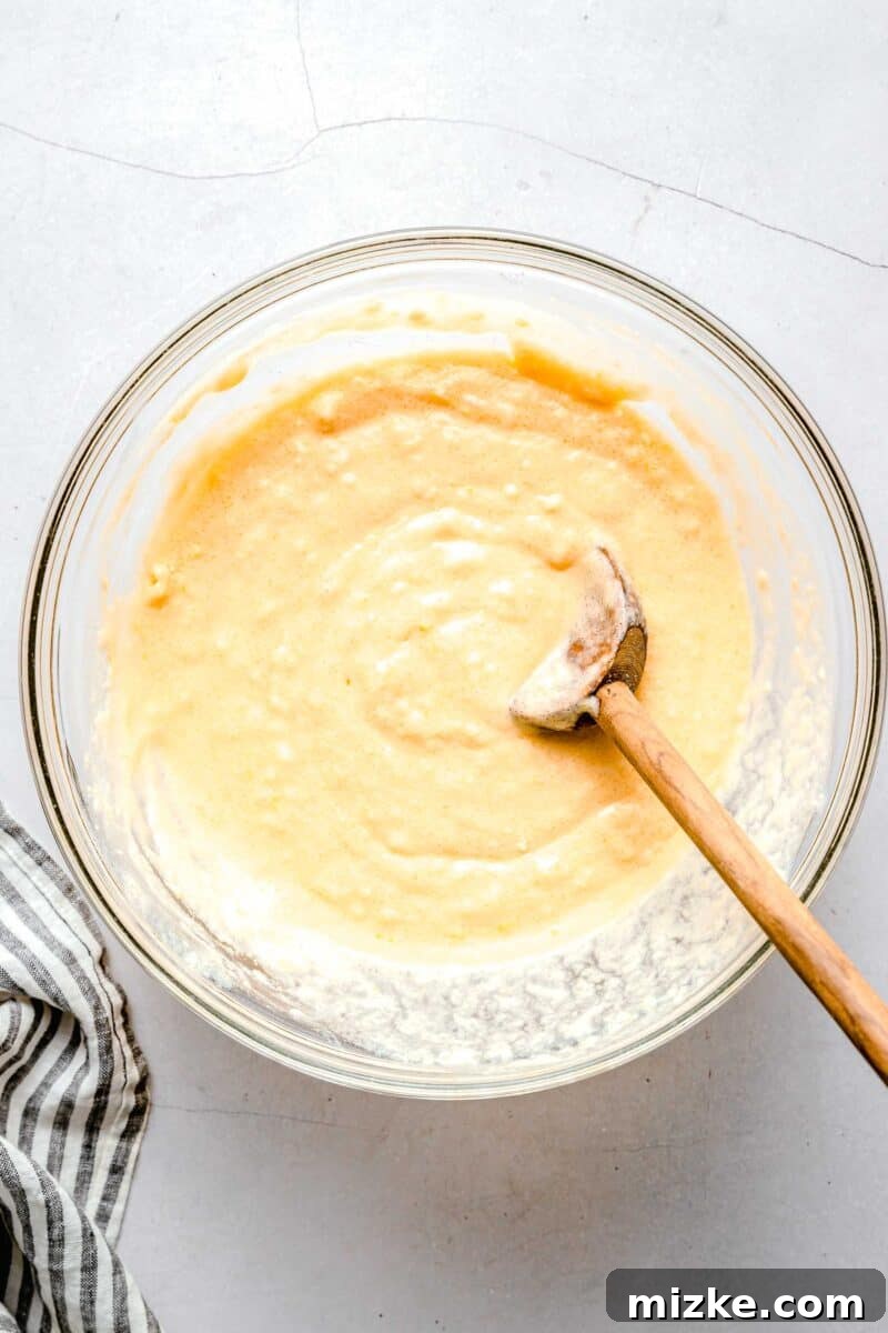 batter for lemon blueberry cupcakes mixed together with a wooden spoon in a clear bowl