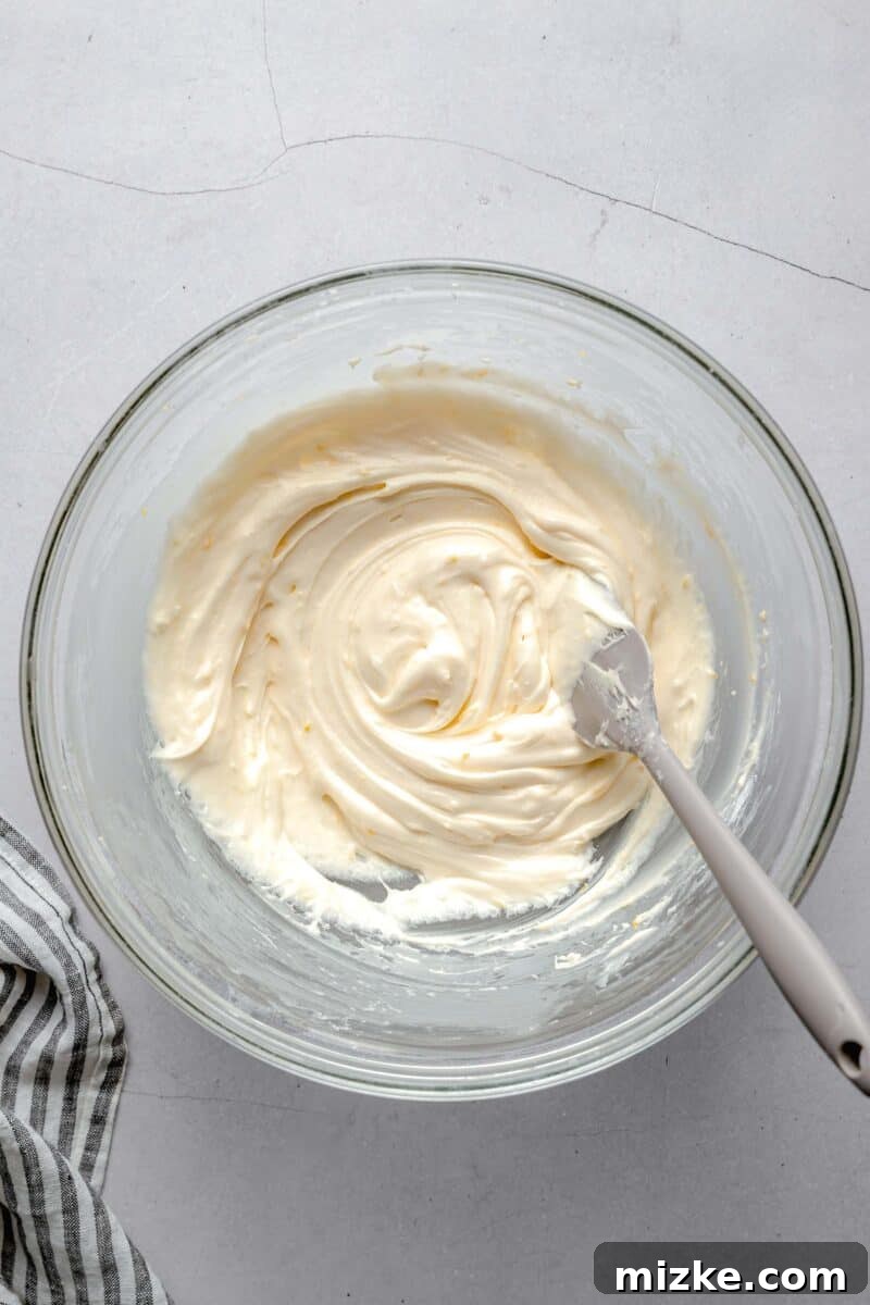 lemon cream cheese frosting in a clear bowl and grey spatula