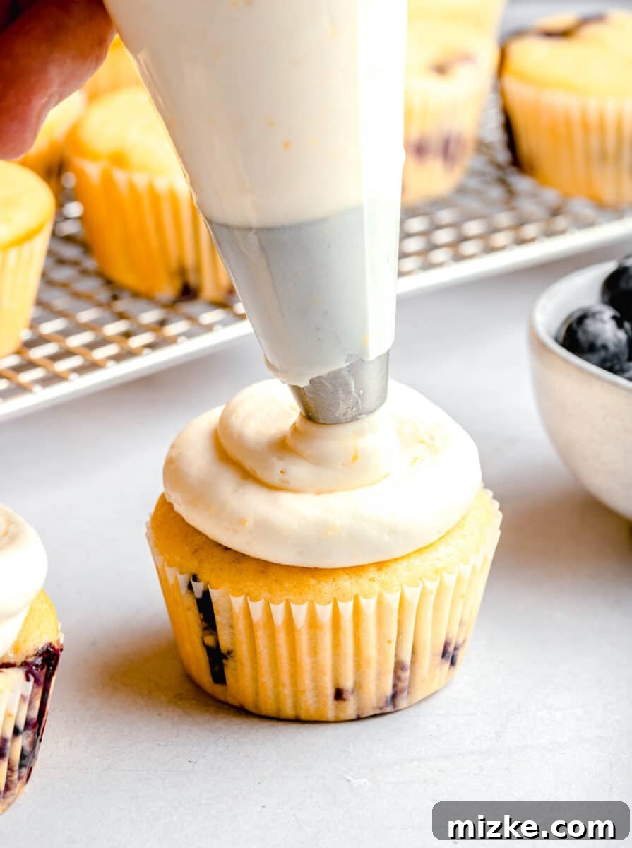 piping lemon cream cheese frosting on a lemon blueberry cupcake