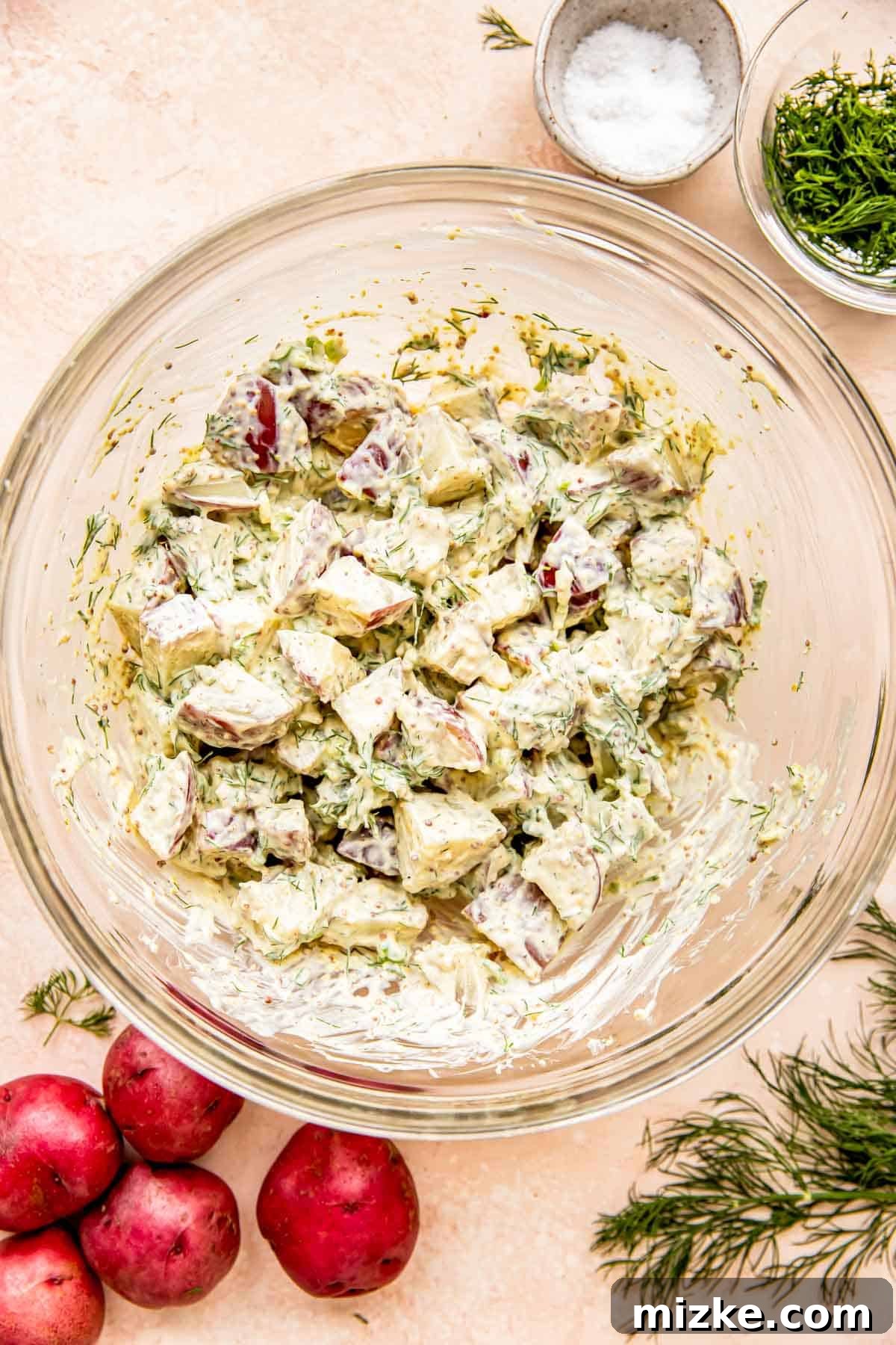 Zesty Dill Potato Salad 7 The creamy dill potato salad is being gently mixed in a spacious glass bowl, ensuring every potato piece is coated in the luscious dressing.