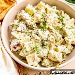 A bowl is filled with creamy potato salad, garnished with fresh dill.