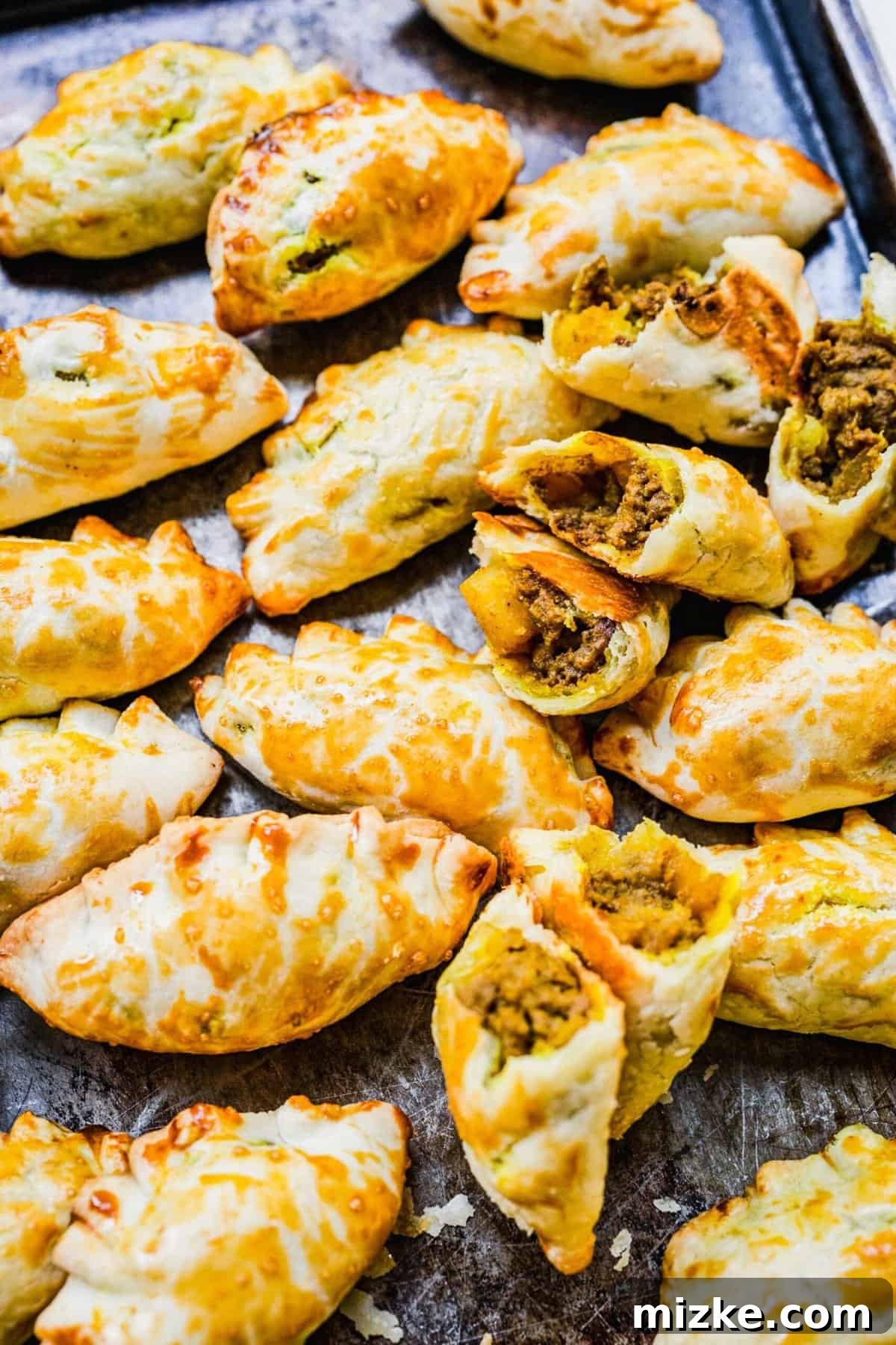 Chinese Curry Pockets are a traditional snack that tucks curried beef and potatoes into circles of dough, then bakes them to flaky perfection! Golden brown Chinese curry pockets on a baking sheet, with some cut open to reveal the rich curried beef and potato filling inside.