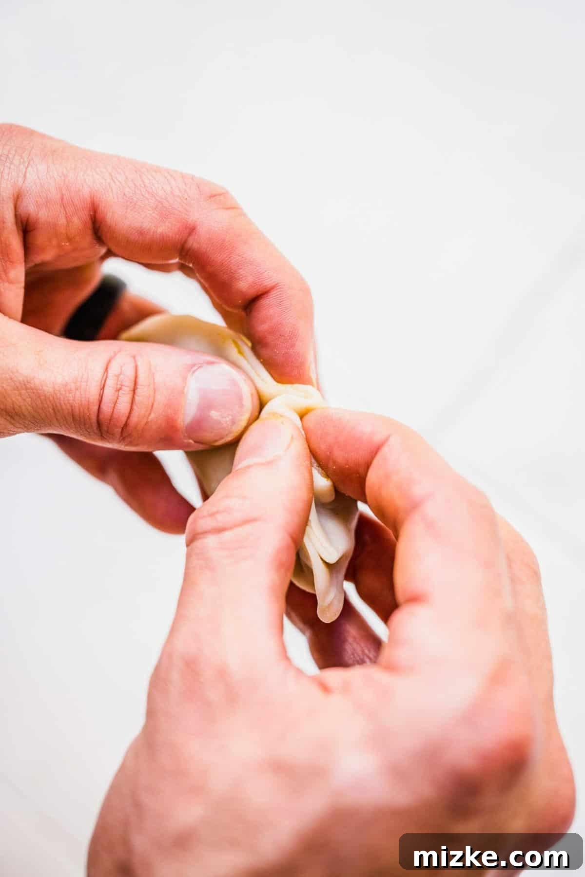 Chinese Curry Pockets are a traditional snack that tucks curried beef and potatoes into circles of dough, then bakes them to flaky perfection! Hands demonstrating the technique of crimping the edge of a Chinese curry pocket, creating a decorative and secure seal.