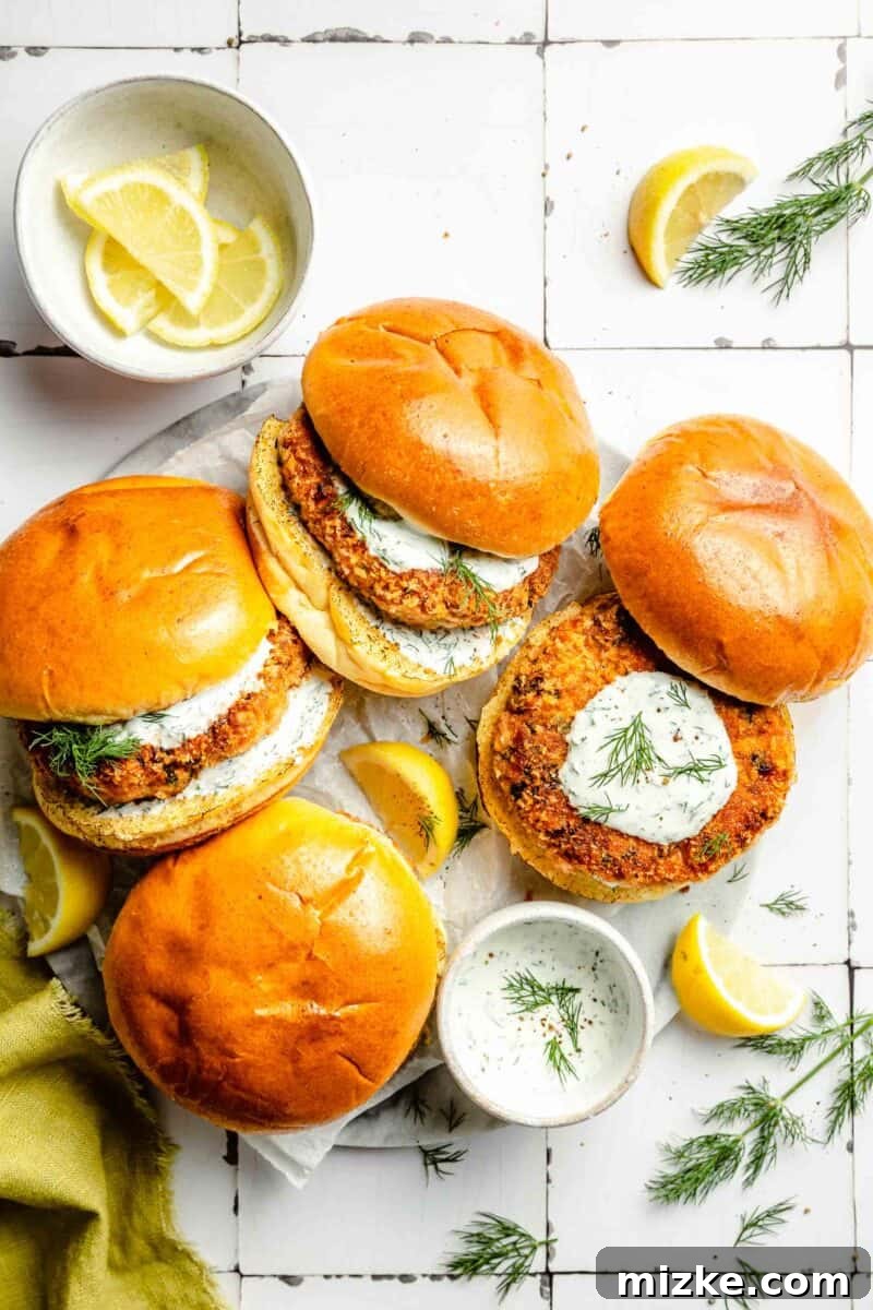 Crispy Air Fryer Salmon Burgers 2 Several golden brown air fryer salmon burgers are artistically arranged next to a bowl of creamy lemon dill mayonnaise and fresh lemon wedges, ready to be served.