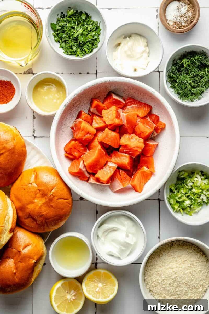 Crispy Air Fryer Salmon Burgers 3 Fresh ingredients for salmon burgers, including raw salmon fillets, panko breadcrumbs, fresh herbs, lemon, and a bowl of mayonnaise, are neatly arranged on a white surface, ready for preparation.