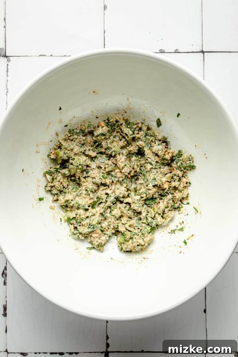 Crispy Air Fryer Salmon Burgers 4 A white bowl contains a vibrant mixture of panko breadcrumbs, chopped fresh parsley, finely diced scallions, and a touch of cayenne pepper, awaiting further ingredients.