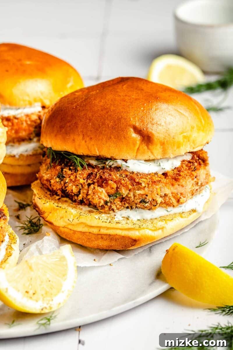 Crispy Air Fryer Salmon Burgers 8 Two beautifully golden-brown air fryer salmon burgers are served on a rustic wooden board next to vibrant green lemon wedges, ready for a fresh and healthy meal.