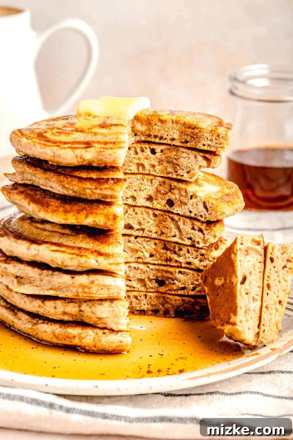 Fluffy Pumpkin Spice Pancakes: The ultimate treat for fall mornings. Light, airy, and bursting with warm autumn spices, they're truly irresistible. A stack of golden-brown pumpkin spice pancakes with a slice taken out, adorned with a melting pat of butter and generously drizzled with rich maple syrup.