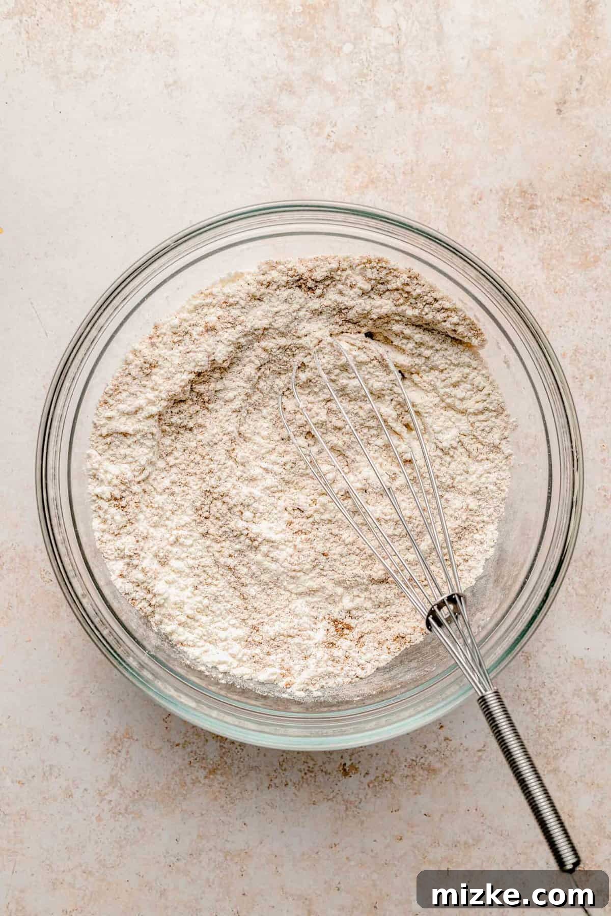 The initial step to perfect pumpkin spice pancakes: gently whisking dry ingredients for a light, fluffy, and absolutely irresistible result. A close-up of a large mixing bowl where dry ingredients for pumpkin pancakes are being whisked together, creating a light, powdery blend.