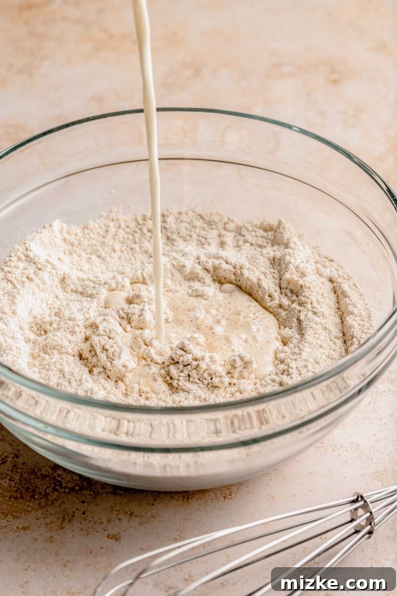 Adding the wet elements to craft the perfect pumpkin spice pancake batter. Light, fluffy, & loaded with pumpkin spice, they're absolutely irresistible. A steady stream of milk being poured into a well created in the center of the dry ingredients in a mixing bowl, for pumpkin pancakes.