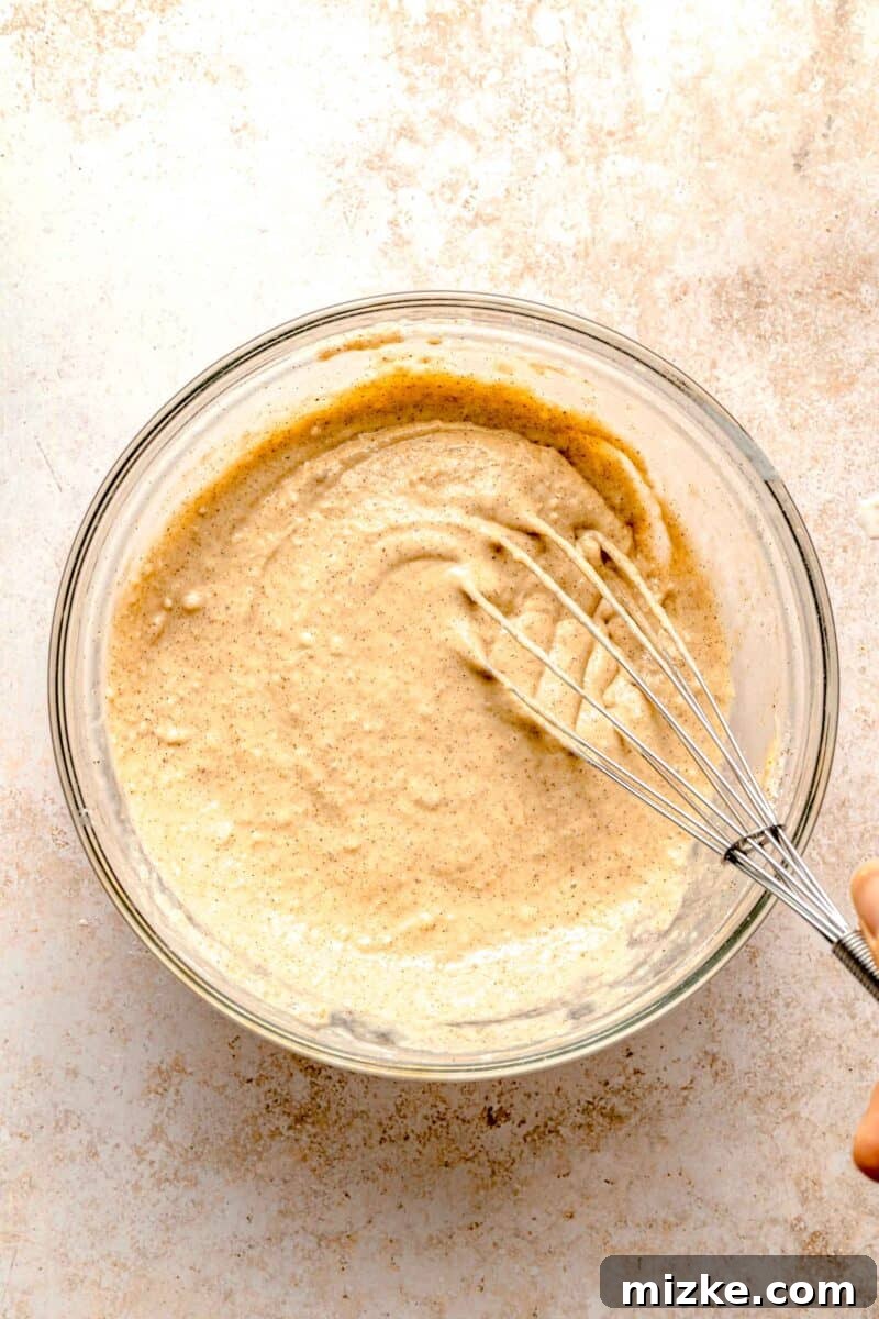 Whisking together the wet and dry ingredients to form the perfect pumpkin spice pancake batter. Light, fluffy, & loaded with pumpkin spice, they're absolutely irresistible. A hand whisking milk, egg, and vanilla extract into the dry ingredients to form the smooth pumpkin pancake batter.