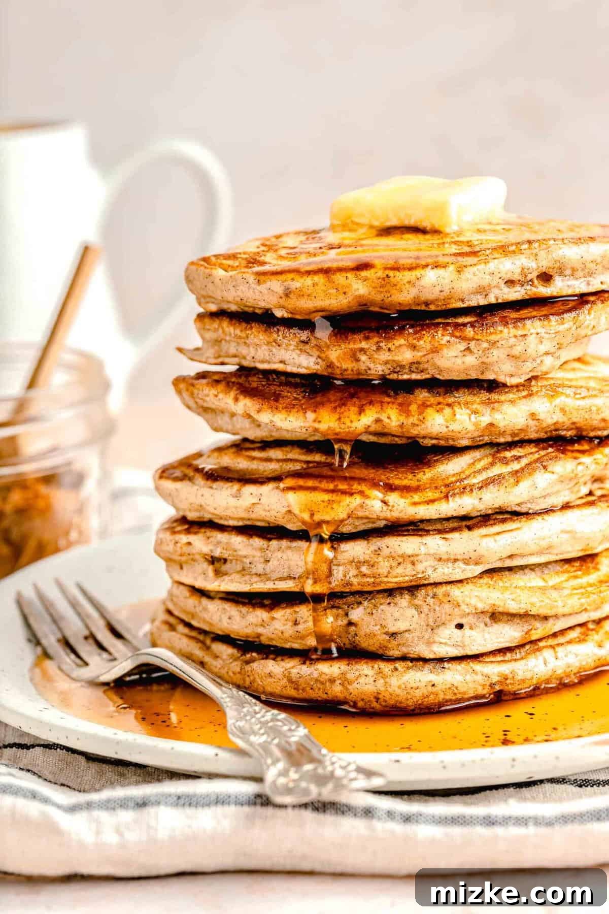 A picture-perfect stack of pumpkin spice pancakes, ready for a cozy fall morning. Light, fluffy, & loaded with pumpkin spice, they're absolutely irresistible. A stack of perfectly cooked pumpkin spice pancakes sits on a plate, topped with a melting pat of butter and drenched in golden maple syrup, ready to be enjoyed.
