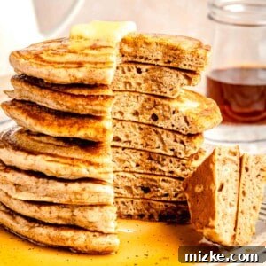 Pumpkin spice pancakes are the perfect treat for fall mornings. Light, fluffy, & loaded with pumpkin spice, they're absolutely irresistible. A stack of pumpkin spice pancakes with a slice taken out of it on a plate topped with butter and dowsed in maple syrup.