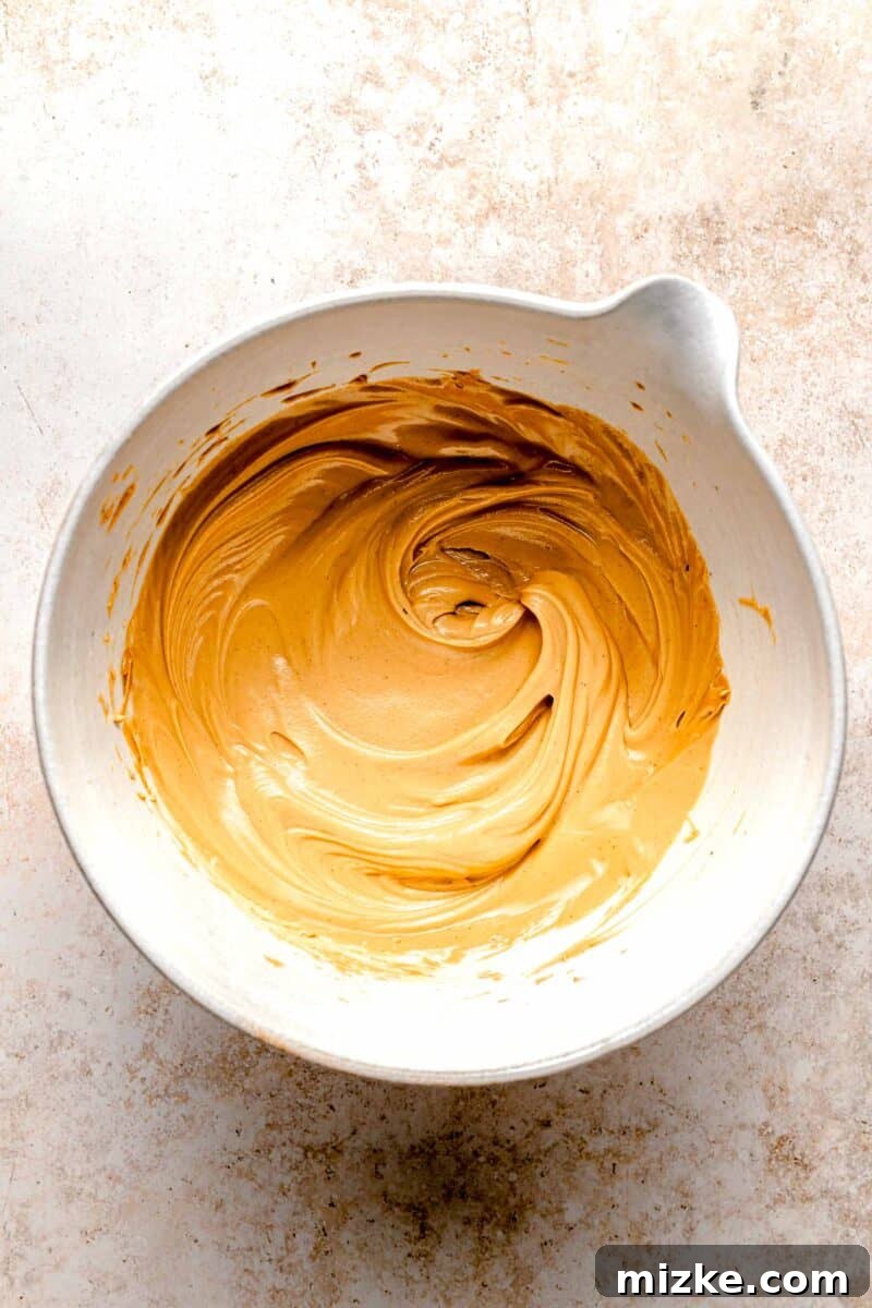 Creamy peanut butter sweetened with powdered sugar is rolled into balls and coated in chocolate to make these decadent peanut butter balls. Creamy peanut butter and softened butter being combined in a bowl, forming a smooth base for the dough.