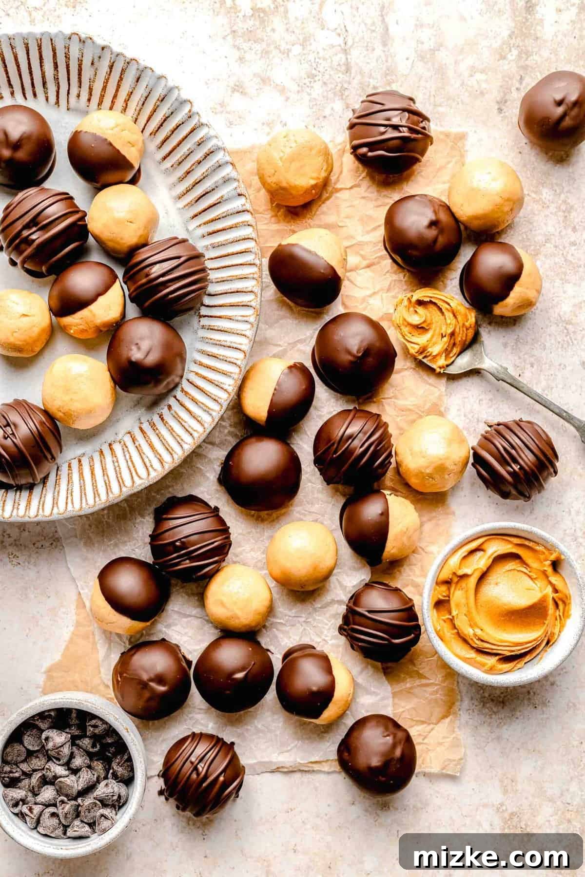Creamy peanut butter sweetened with powdered sugar is rolled into balls and coated in chocolate to make these decadent peanut butter balls. An overhead view of finished chocolate-covered peanut butter balls, artfully arranged near small ramekins holding peanut butter and chocolate chips, highlighting the key ingredients.