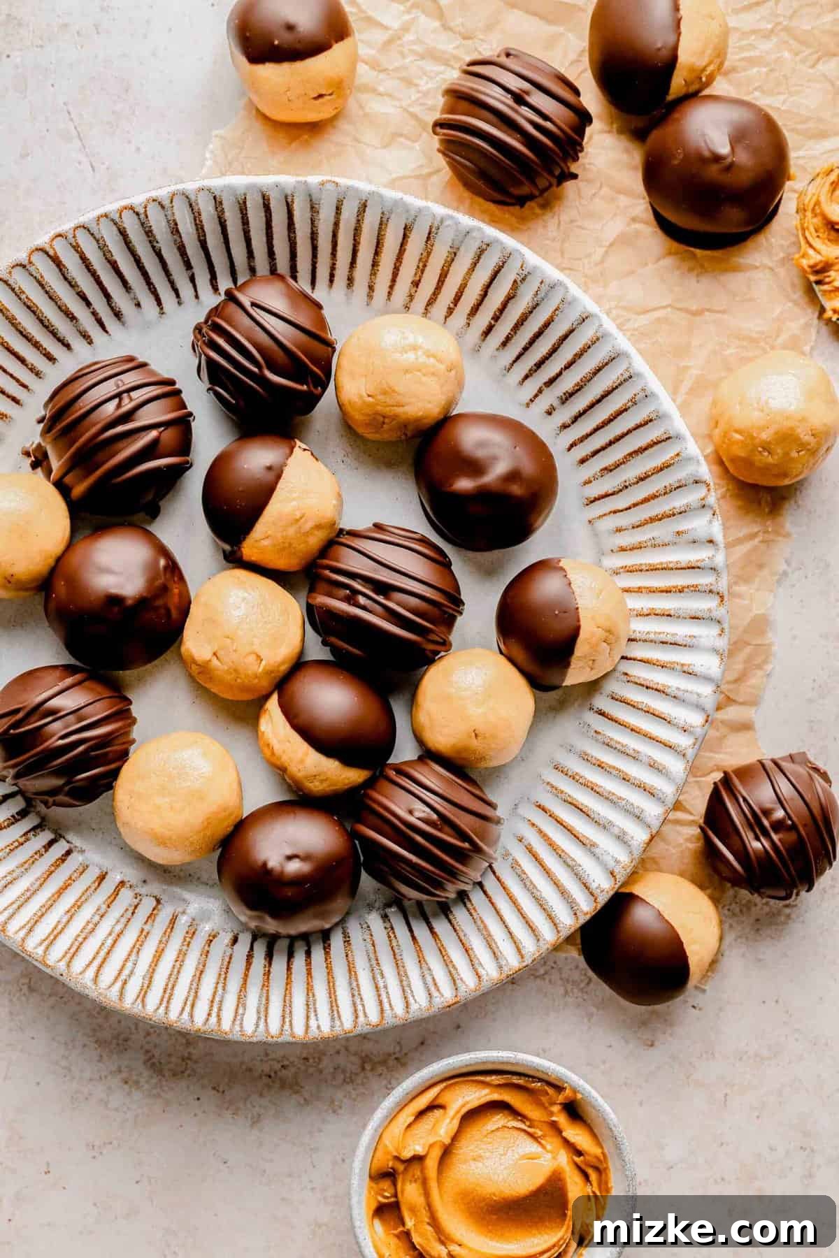Creamy peanut butter sweetened with powdered sugar is rolled into balls and coated in chocolate to make these decadent peanut butter balls. An inviting overhead photograph of several finished chocolate-covered peanut butter balls arranged on a plain plate, showcasing their perfect shape and glossy coating.