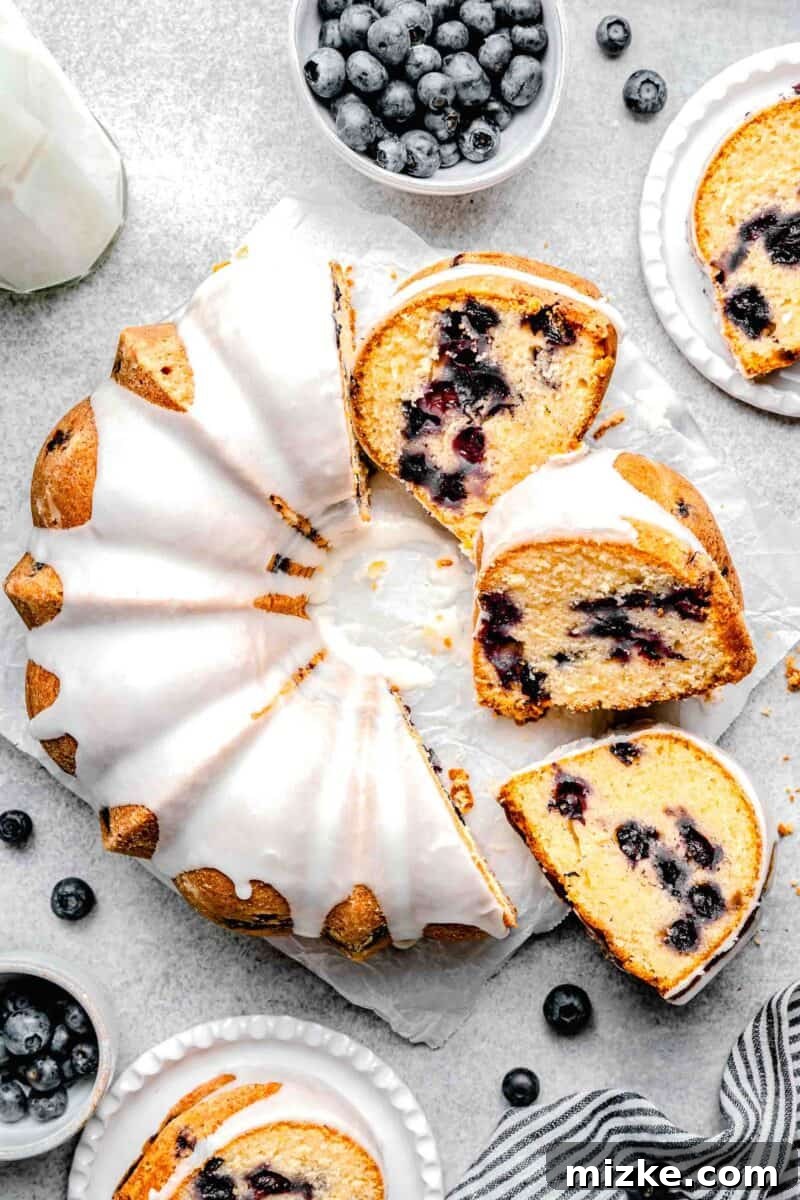 Blueberry Burst Bundt 2 Several slices of blueberry bundt cake beautifully arranged next to half of a whole glazed cake, showcasing its moist interior and fruit distribution.