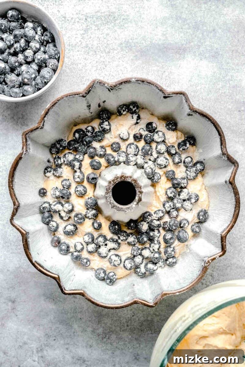 Blueberry Burst Bundt 6 A layer of fresh blueberries carefully scattered over a portion of cake batter in a prepared bundt pan, ensuring even distribution throughout the cake.
