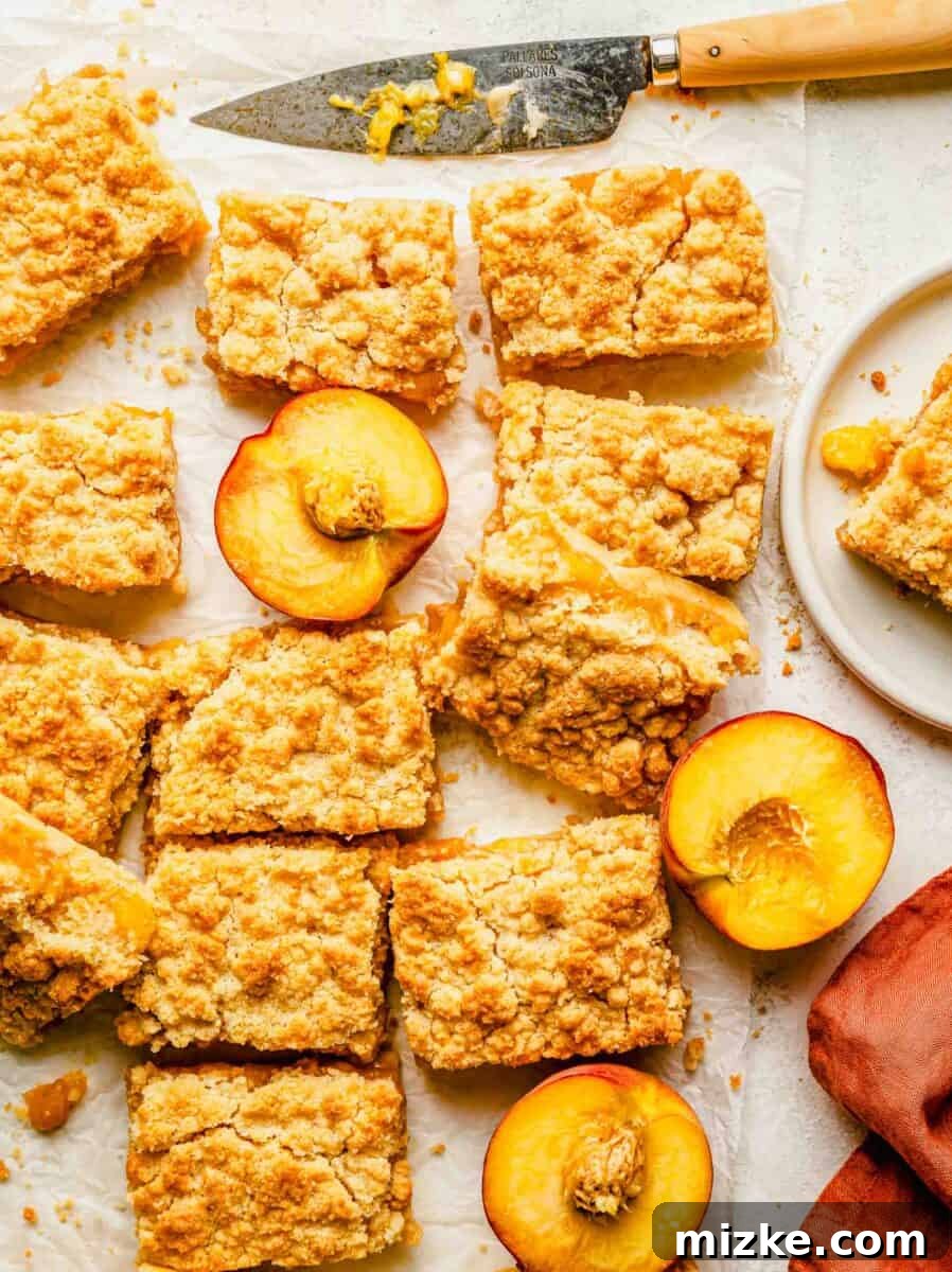 Golden Peach Crumble Squares 2 A generous serving of perfectly sliced peach crumble bars, showcasing their golden crust and juicy filling, presented alongside fresh halved peaches.