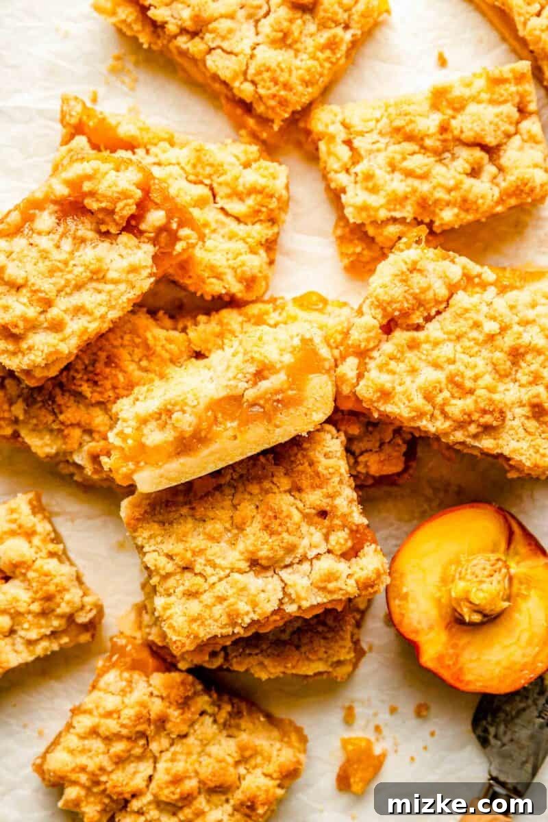 Golden Peach Crumble Squares 3 A beautifully halved peach rests next to a cluster of delicious peach crumble bars, highlighting the fresh fruit inspiration behind the dessert.