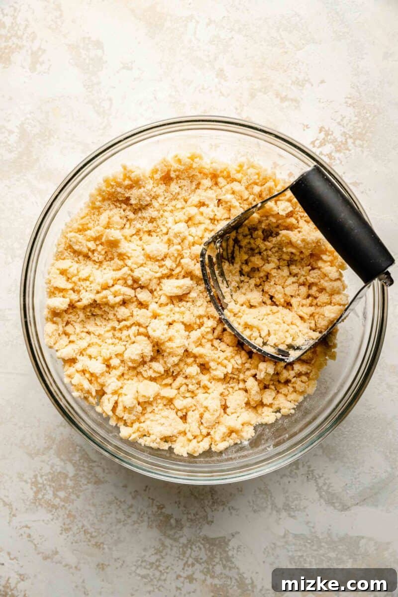 Golden Peach Crumble Squares 5 The process of cutting cold butter into a flour mixture using a pastry blender, creating fine, pea-sized crumbs for the dough.
