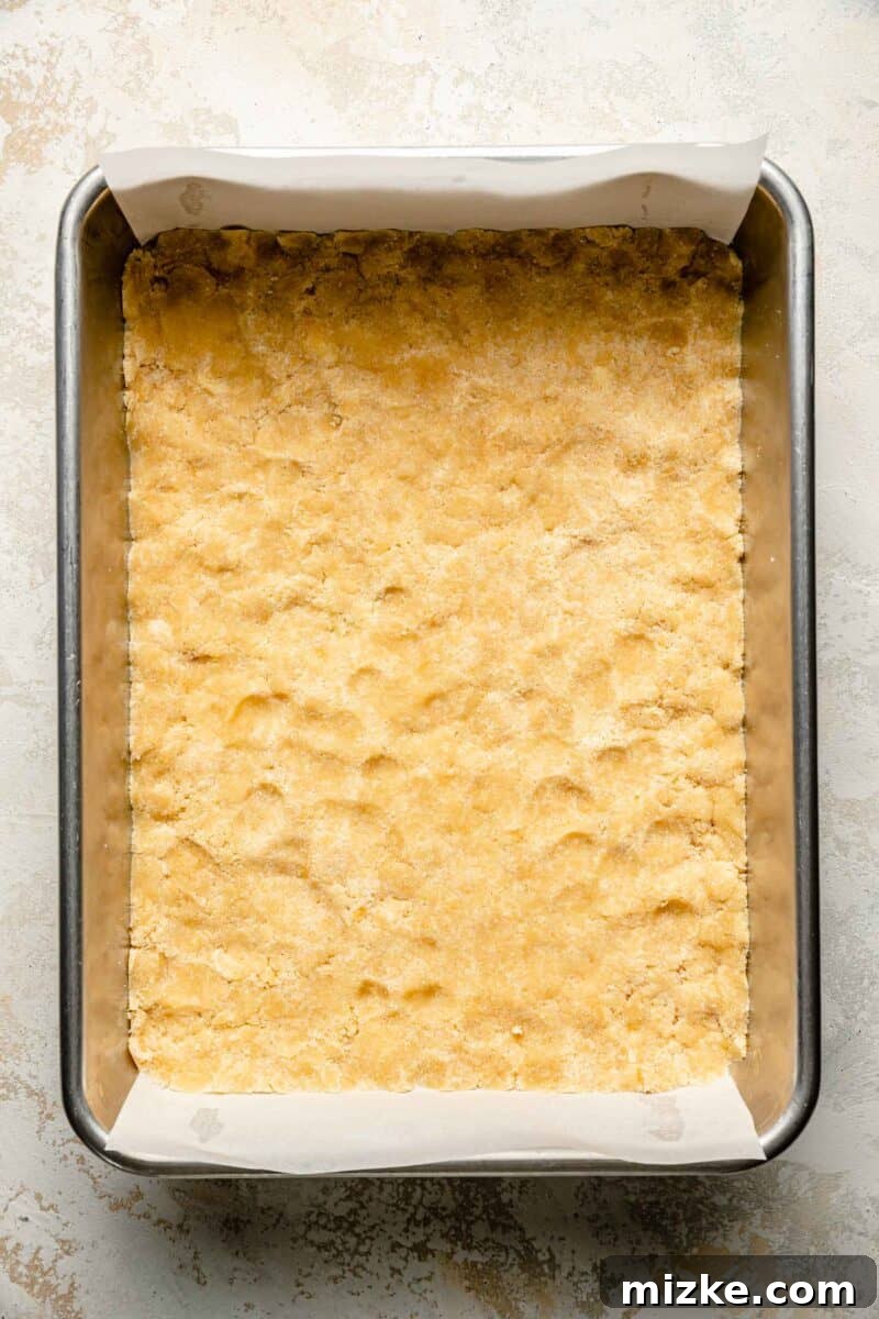 Golden Peach Crumble Squares 6 Half of the crumbly dough is evenly pressed into the bottom of a parchment-lined 9x13 inch baking pan, forming the base layer.