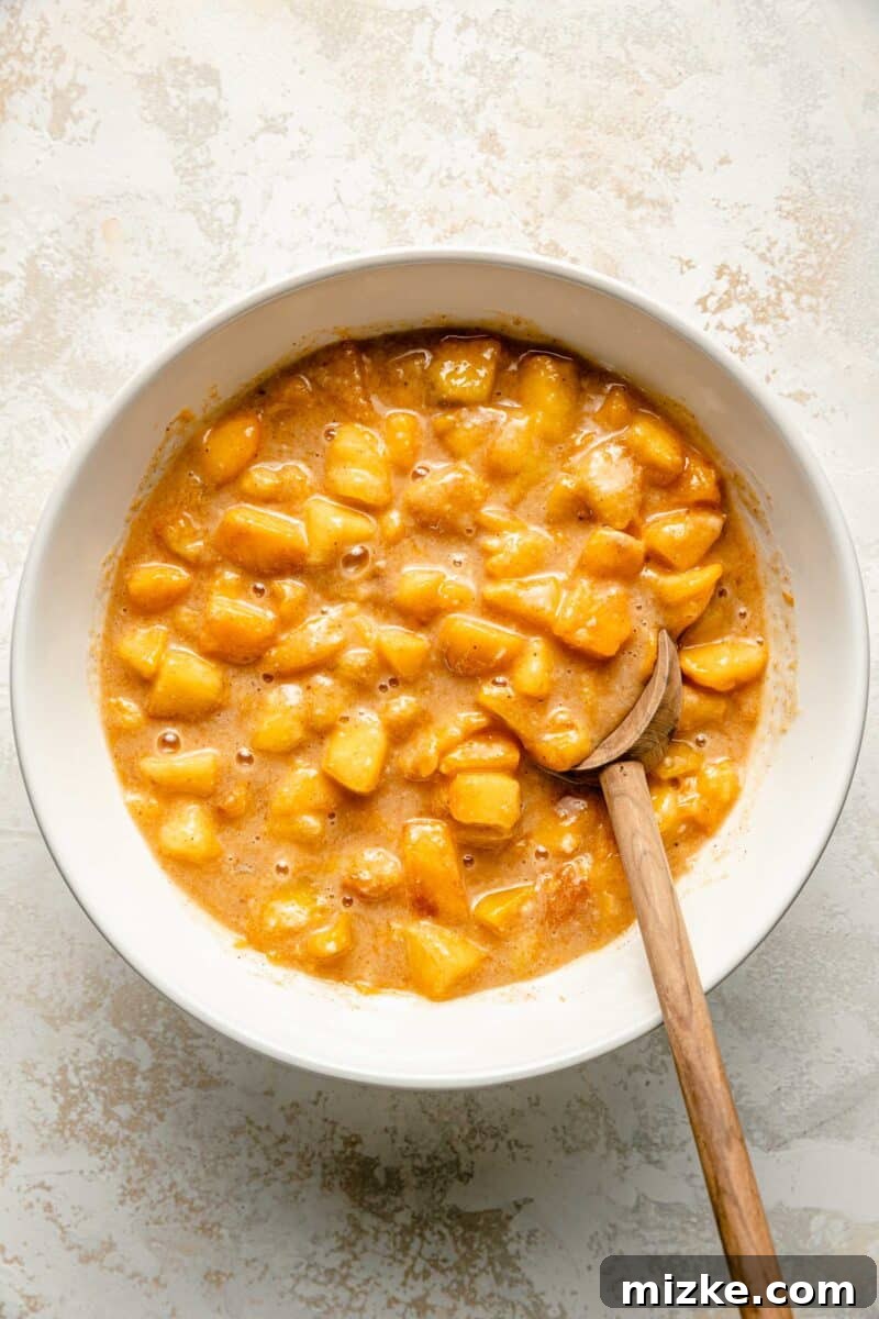 Golden Peach Crumble Squares 7 A spoon gently stirs a vibrant peach filling mixture in a white bowl, combining fresh peaches with sugar and lemon juice.