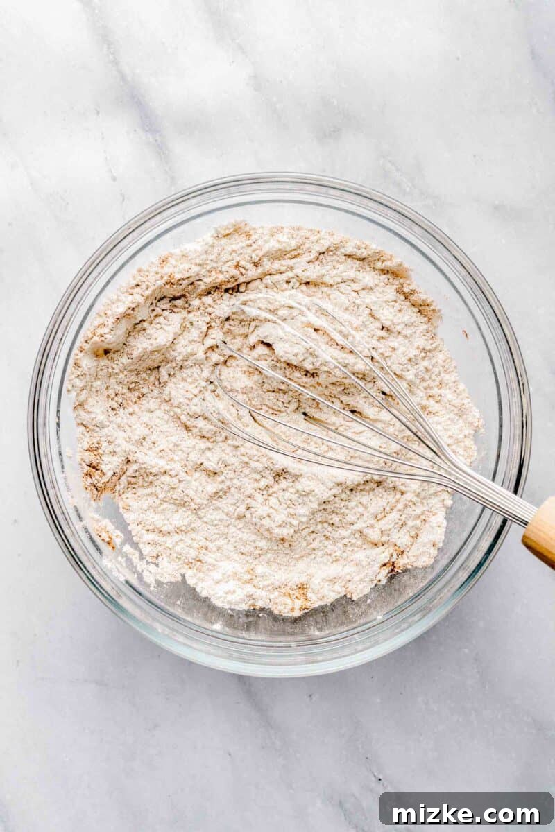 Whisking together dry ingredients for sweet potato bread to ensure even distribution and a light texture. A bowl containing dry ingredients like flour, baking soda, baking powder, and salt, being whisked together for sweet potato bread.