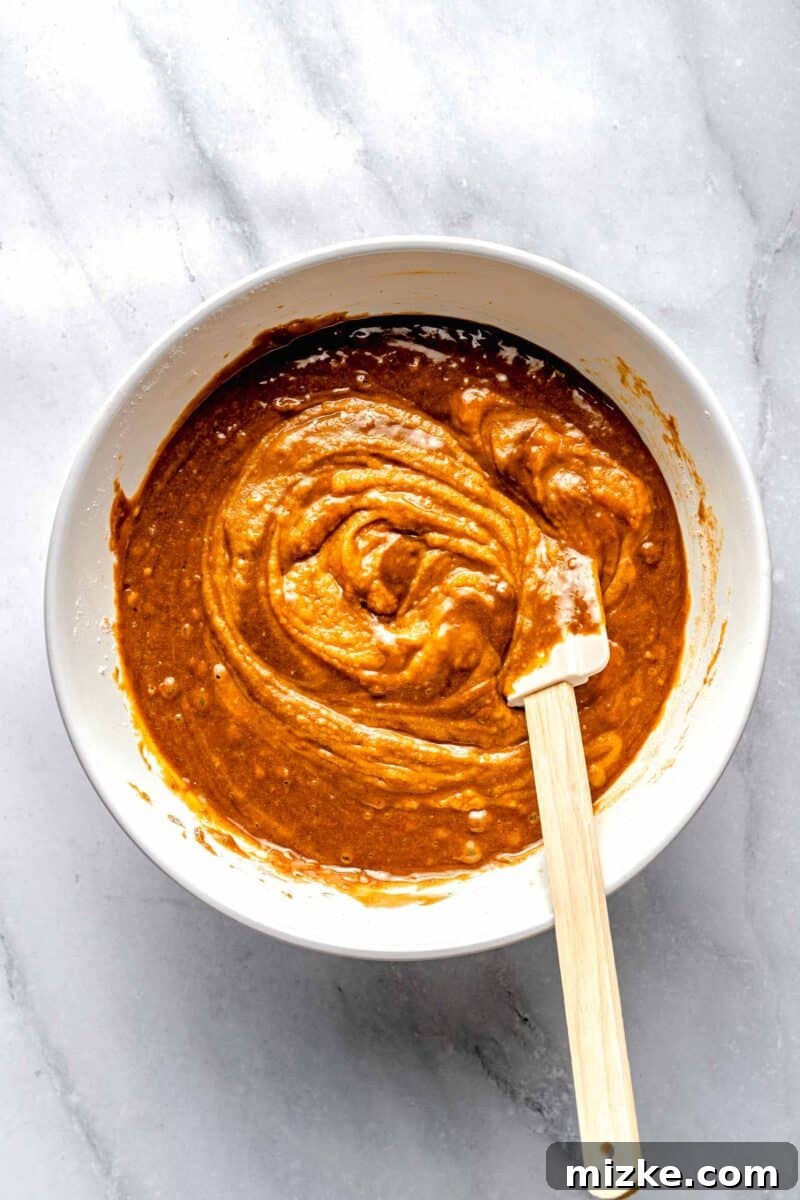 Combining wet and dry ingredients with buttermilk for sweet potato bread, ensuring a perfectly mixed batter. The process of gently folding dry ingredients into wet ingredients, alternating with buttermilk, to create the sweet potato bread batter.