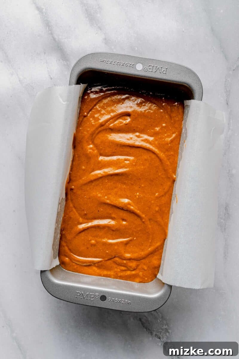 Sweet potato bread batter filling a parchment-lined loaf pan, poised for its transformation in the oven. Sweet potato bread batter carefully poured into a loaf pan lined with parchment paper, ready for baking.